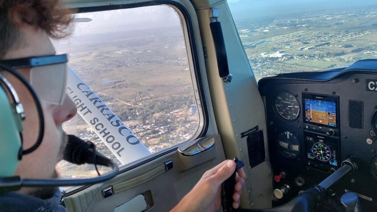 Piloto con headset en cabina durante un vuelo, con instrumentos y paisaje aéreo visibles por la ventana